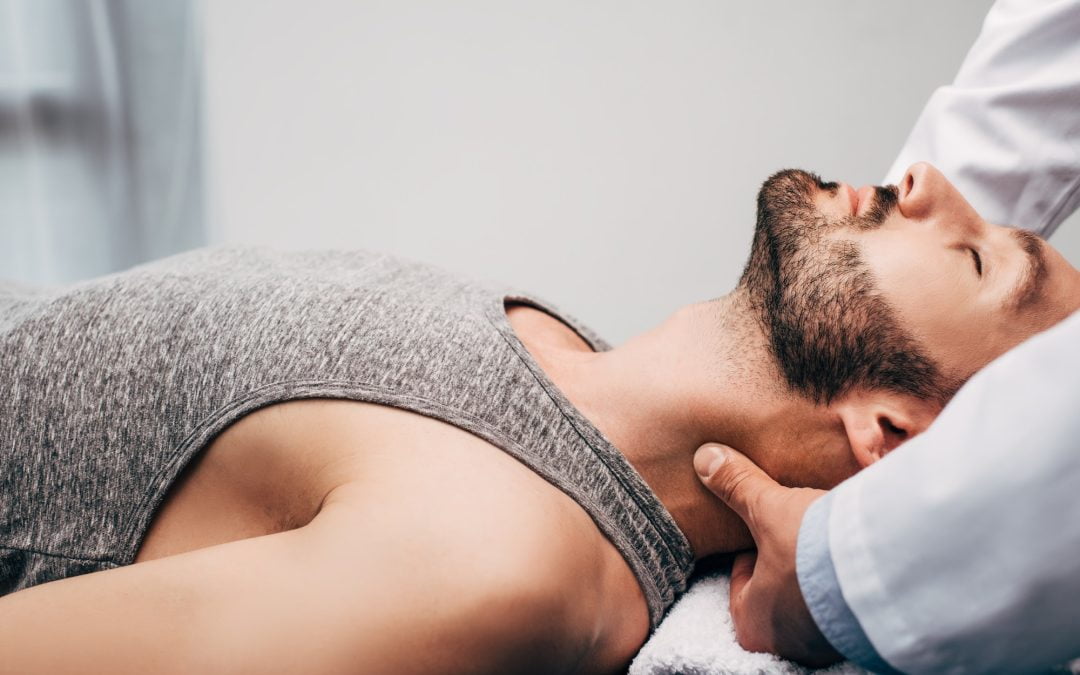 chiropractor massaging neck of man lying on towel in hospital