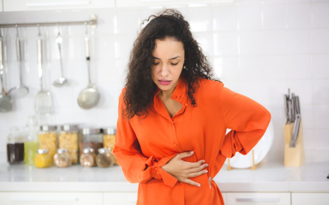 woman with curly hair standing in modern kitchen taking support of counter holding her abdomen hard