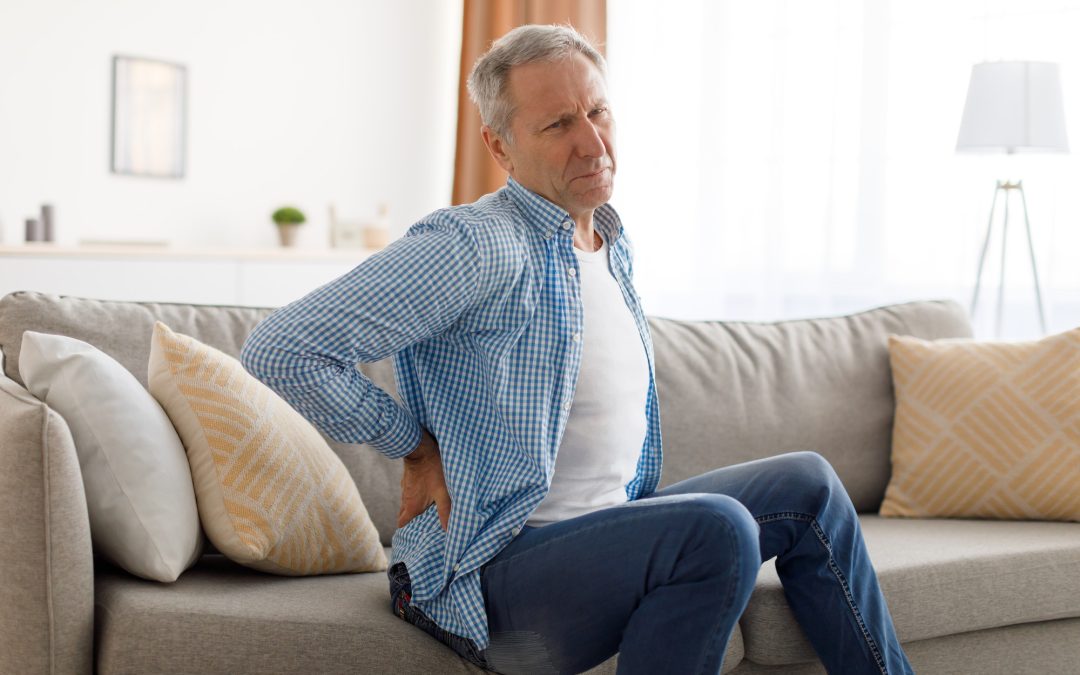 Mature man with back pain sitting on couch at home