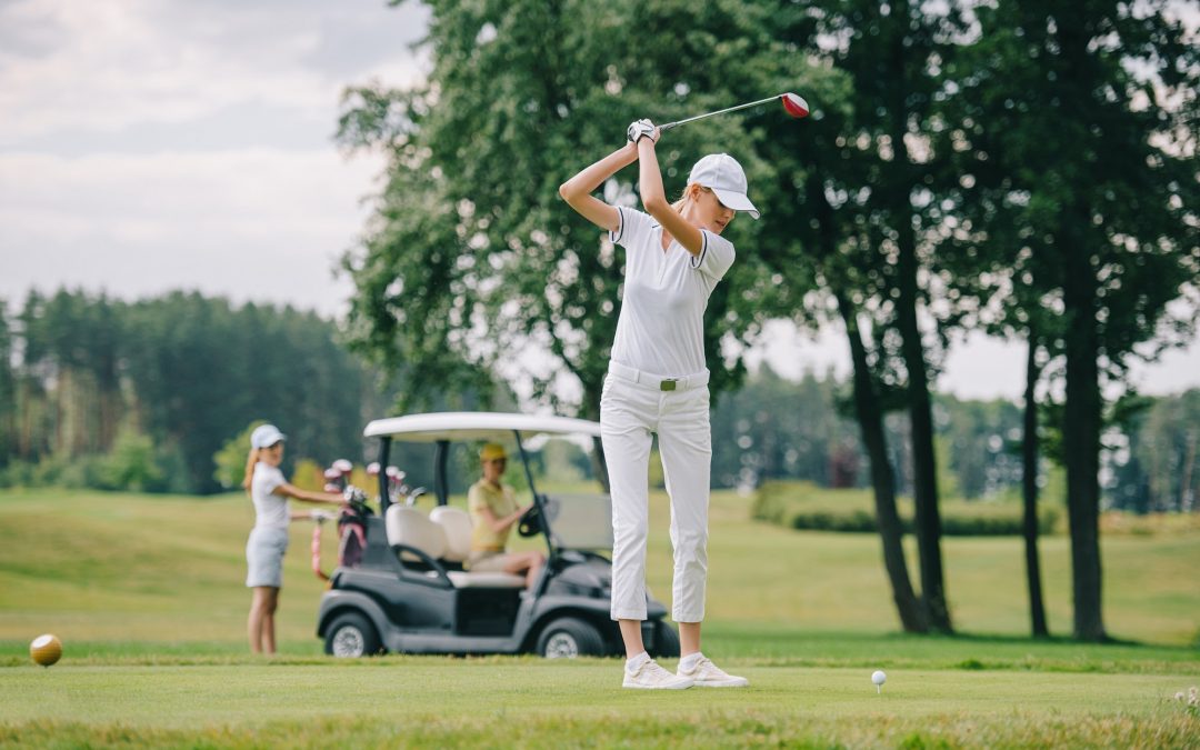 selective focus of woman with golf club playing golf and friends resting at golf cart on green lawn