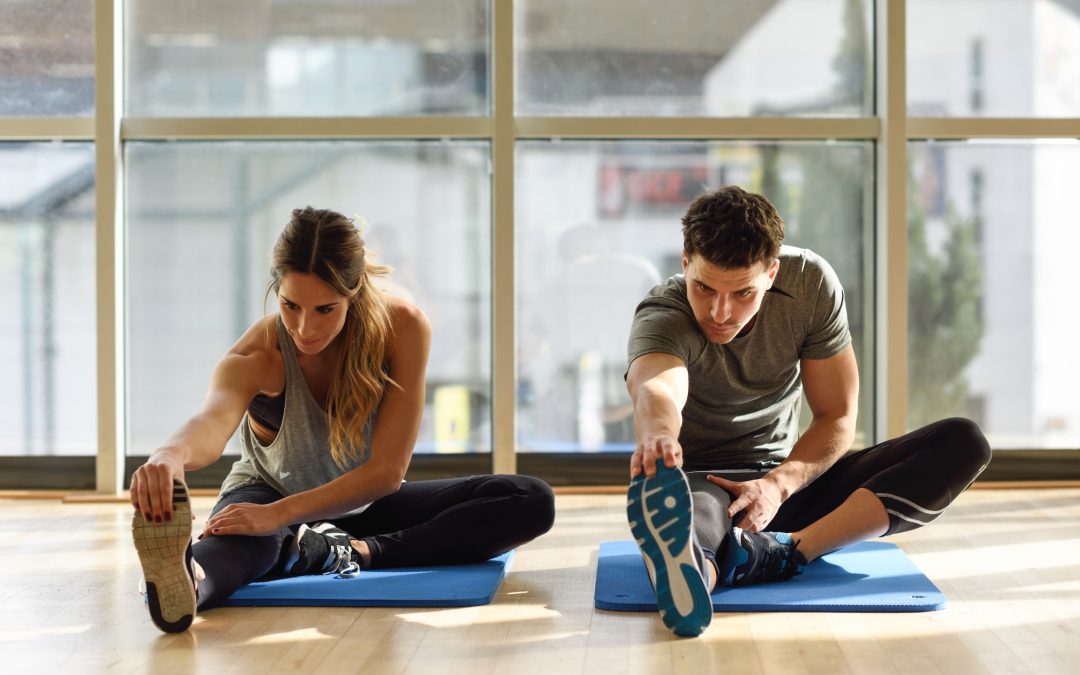 Two people streching their legs in gym.