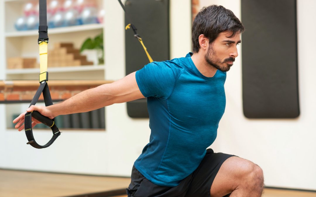 Muscular sportsman stretching shoulders on TRX straps