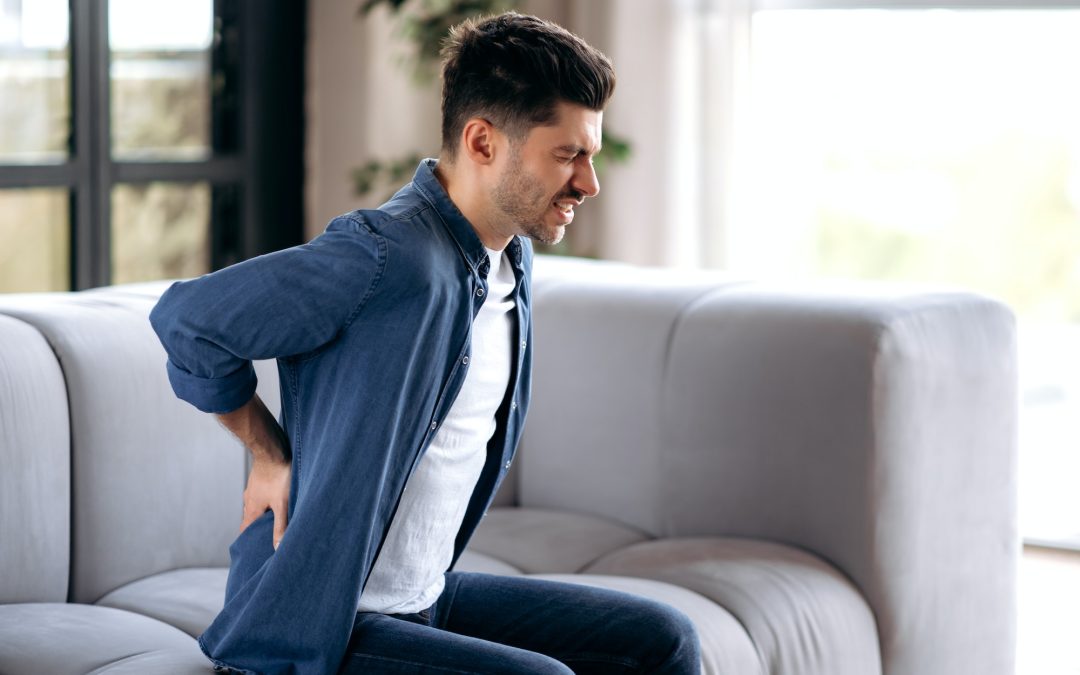 Sad upset young adult caucasian bearded man, in casual clothes, sitting on the sofa in the living